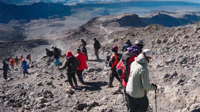 Vandrare p&aring; en stenig sluttning ovanf&ouml;r molnen p&aring; Kilimanjaro